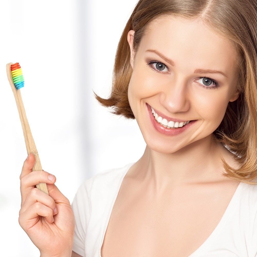 Девушка держит в руке бамбуковую зубную щетку радужного цвета