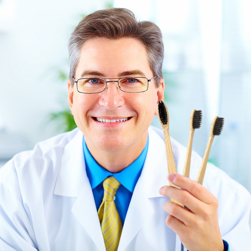 Стоматолог держит в руках 3 бамбуковые зубные щетки